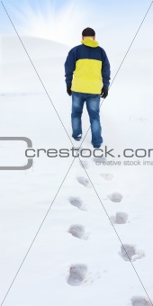 Man in yellow jacket walking on snow, footprints in snow, behind