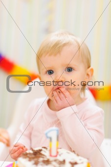 Portrait of eat smeared baby eating first birthday cake