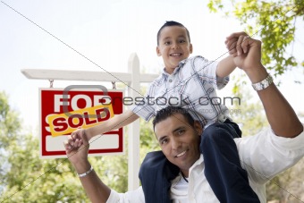 Excited Hispanic Father and Son in Front of Sold For Sale Real Estate Sign.