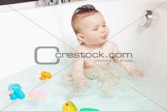 Cute baby playing with water and showing tongue while taking a bath