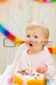 Surprised baby eating first birthday cake
