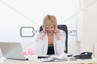 Stressed middle age business woman sitting at office table