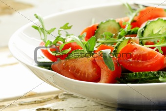 fresh arugula salad with tomatoes, cucumbers in a white plate