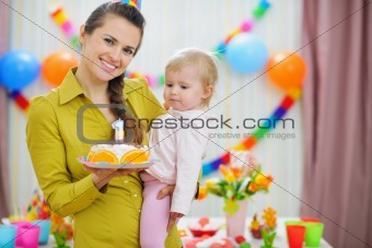 Mother holding baby and birthday party cake