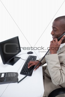 Side view of a male secretary answering the phone while using a computer