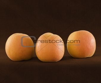 Three Ripe Organic Apricots On Brown Backround