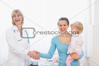 Happy mother holding baby and shaking hand to pediatric doctor