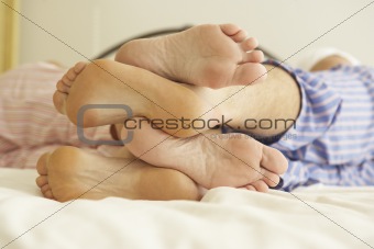 Close Up Of Couple's Feet Relaxing On Bed At Home