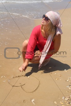 Beautiful woman at the beach drawing heart on the sand