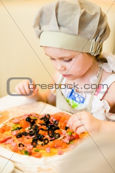 Little girl adding ingredients in pizza