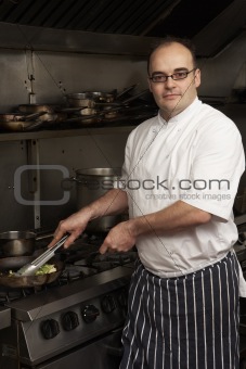 Male Chef Preparing Meal On Cooker In Restaurant Kitchen