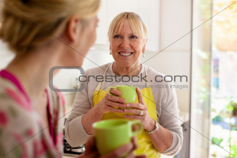 Mother and daughter talking, drinking coffee in kitchen