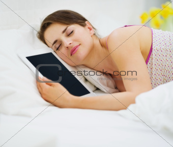 Happy woman sleeping embracing tablet PC