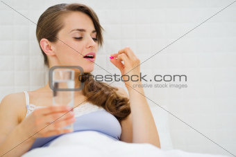Woman in bed taking pills