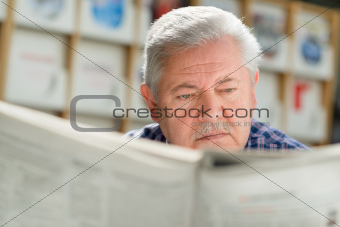 Elderly man with mustache reading paper in library