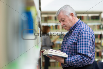 old man reading and choosing book in library