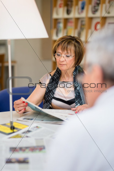 Old woman reading newspaper with husband in library