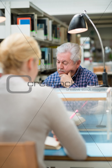 Senior man studying among young people in library