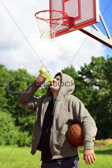 Man holding basketball and drink from bottle of water