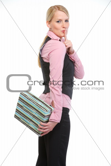 Woman holding present box behind back and showing shh gesture
