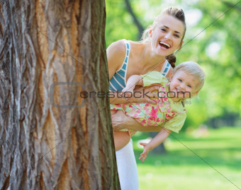 Smiling mother and baby looking out from tree