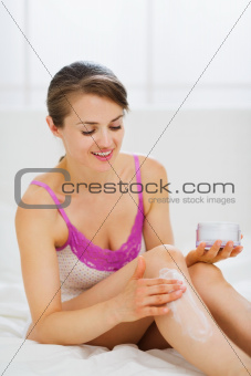 Self caring woman applying creme on leg