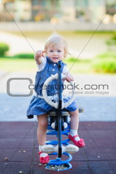 Baby swing on horse on playground and pointing in camera
