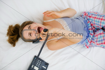 Excited girl laying on bed and speaking phone. Upper view