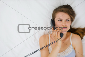Portrait of girl laying on bed and speaking phone. Upper view