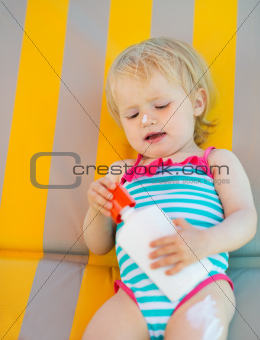 Baby laying on sun bed with sun block bottle