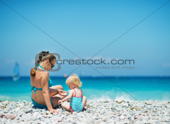 Mother playing with baby on beach. Rear view