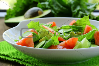 fresh salad with avocado and tomato on a wooden table