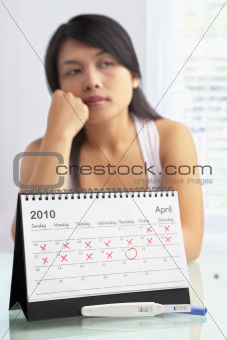 Sad woman with negative pregnancy test and calendar