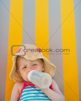 Baby laying on sun bed and drinking from bottle