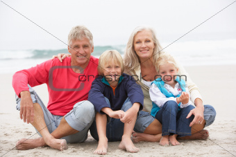 Grandparents And Grandchildren Sitting On Winter Beach Together