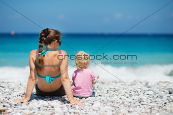 Mother sitting with baby on beach. Rear view