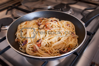 Spaghetti with clams into frying pan on stoves