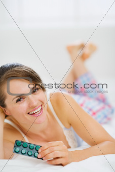 Happy woman laying on bed with pack of pills