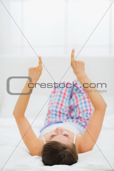 Woman laying on bed and pointing on copy space. Rear view