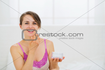 Healthy woman applying creme on face in bedroom