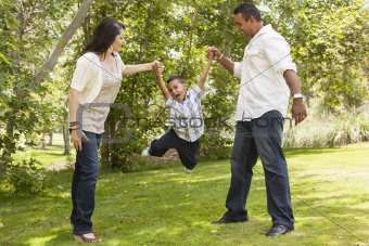 Happy Hispanic Mother and Father Swinging Son in the Park.