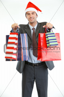 Smiling businessman in Santa's hat showing shopping bags