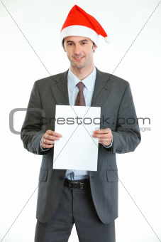 Smiling businessman in Santa's hat showing blank paper