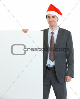 Smiling businessman in Santa's hat showing blank billboard