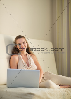 Portrait of happy young woman sitting on sofa with laptop