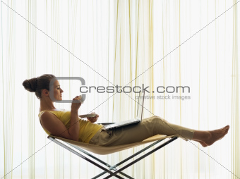 Young woman with coffee cup using laptop at home