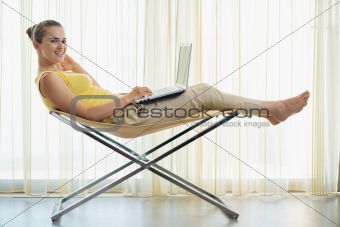 Happy young woman sitting on modern chair and working on laptop
