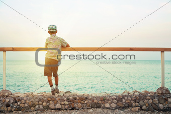 boy standing on quay in the dusk looking at sea