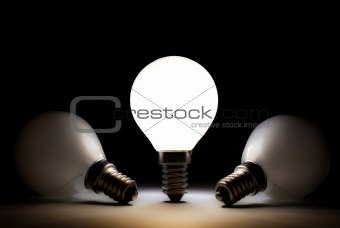 One light bulb shining in a dark space with other dead bulbs
