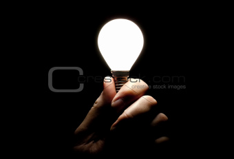 Lit lightbulb held in hand on black background